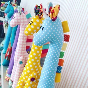 Könnte beinhalten: Eine Reihe von bunten, handgefertigten Stofftieren in Giraffenform mit Punkten. Die Giraffen sind aus weichem Stoff gefertigt und haben verschiedene farbige Akzente.