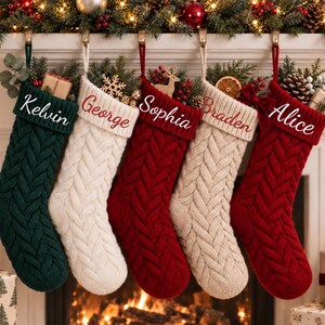 May include: Five knitted Christmas stockings hanging in a row, featuring a cable knit pattern and personalised names embroidered on the cuffs. The stockings are coloured in dark green, cream, red, beige, and red, each filled with festive greenery.