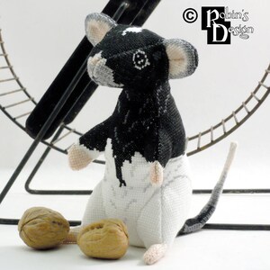 May include: A black and white crocheted mouse toy with a long tail, sitting on a white surface with two walnuts beside it.