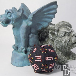 May include: A black and red 20-sided dice with white numbers, sitting on a blue and grey stone gargoyle statue. The dice is made of fabric and has a stitched design.