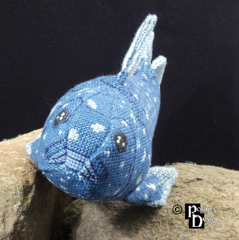 May include: A blue and white plush toy shaped like a fish with black eyes. The fish has a spotted pattern and a white fin.