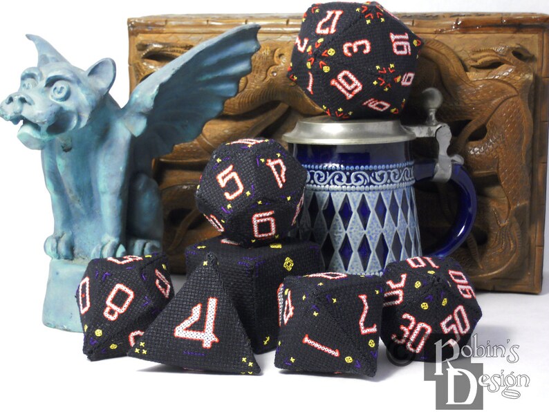 K&ouml;nnte beinhalten: Ein Satz schwarzer W&uuml;rfel mit roten und gelben Zahlen, einige sind dreieckig, andere w&uuml;rfelf&ouml;rmig. Die W&uuml;rfel liegen auf einer wei&szlig;en Oberfl&auml;che vor einer Holzkiste und einem blau-wei&szlig;en Krug.