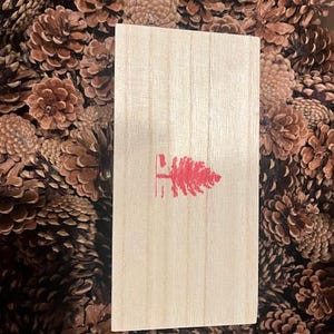 May include: A wooden box with a red pine tree logo on the front. The box is surrounded by pine cones.