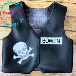 K&ouml;nnte beinhalten: Schwarze Kunstlederweste mit einem wei&szlig;en Totenkopf- und Knochenkreuz-Design auf der linken Seite und einem wei&szlig;en Patch mit dem Namen "BOWEN" auf der rechten Seite.