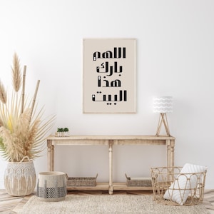 Op de afbeelding: Een ingelijste print met zwarte Arabische kalligrafie op een beige achtergrond. De print hangt boven een houten console met decoratieve manden en een lamp. De kamer is ingericht in neutrale tinten met natuurlijke texturen.