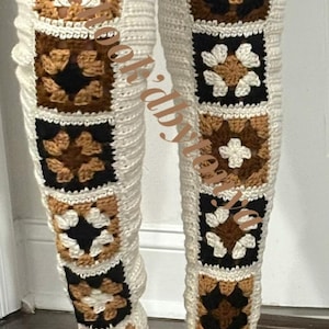 Könnte beinhalten: Ein Paar weiße, gehäkelte Oberschenkelsocken mit braunen und schwarzen Granny Squares. Die Socken haben ein Blumenmuster.