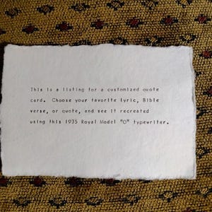 May include: A rectangular white card with deckled edges featuring black typewriter text that reads: This is a listing for a customized quote card. Choose your favorite lyric, Bible verse, or quote, and see it recreated using this 1935 Royal Model O typewriter.