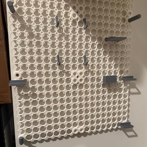 May include: White pegboard with a grid pattern and various gray hooks and shelves attached.