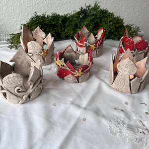 Può includere: Cinque portacandele in ceramica a forma di corona con accenti rossi e dorati. I portacandele sono decorati con fantasiosi disegni di case e stelle.