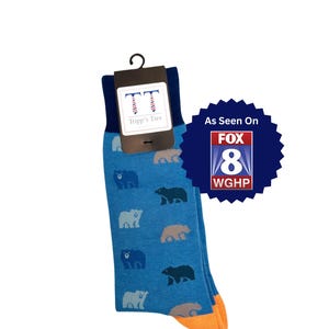 blue socks with orange toe and heel cap with bear motif in shades of blue, green and tan. Text says "100% of proceeds will help animals displaced from Hurricane Helene" and "As Seen on Fox 8 WGHP"