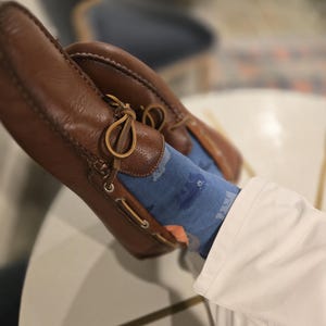 May include: Brown leather boat shoes with blue and white patterned socks. The socks feature a design of small fish.