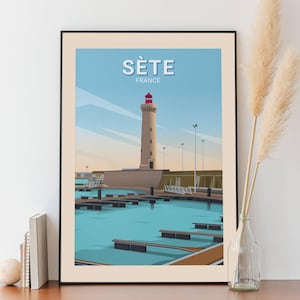 May include: A framed art print depicting the lighthouse of Sète, France. The image shows a beige lighthouse with a red top, set against a blue sky and turquoise water. The word "SÈTE" is displayed at the top of the print.