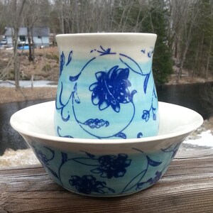 May include: A blue and white ceramic bowl with a matching mug. The bowl and mug feature a floral design with blue flowers and leaves on a white background with a light blue gradient.