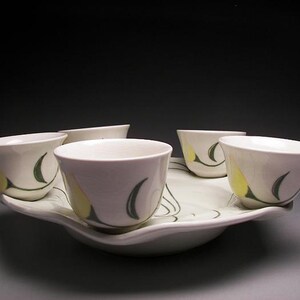 Peut inclure: Un plateau de service en céramique blanche avec cinq petites tasses blanches ornées de motifs floraux jaunes et verts. Les tasses sont disposées en cercle autour du plateau.