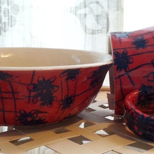 May include: Two red ceramic bowls with black floral designs. The larger bowl is a serving bowl and the smaller bowl is a mug.