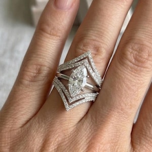 Peut inclure: Une bague de fiançailles en diamant taille marquise avec un anneau en forme de chevron unique, sertie de petits diamants d'appoint. La bague est présentée sur une main, mettant en valeur son design complexe et son éclat. Symbole d'engagement et d'amour.
