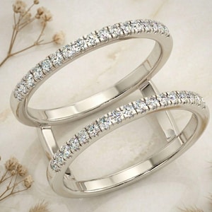 Puede incluir: Dos anillos de plata con una fila de pequeñas piedras preciosas transparentes. Los anillos se muestran sobre una superficie clara, con pequeñas flores secas en el fondo. Anillos de boda o compromiso.