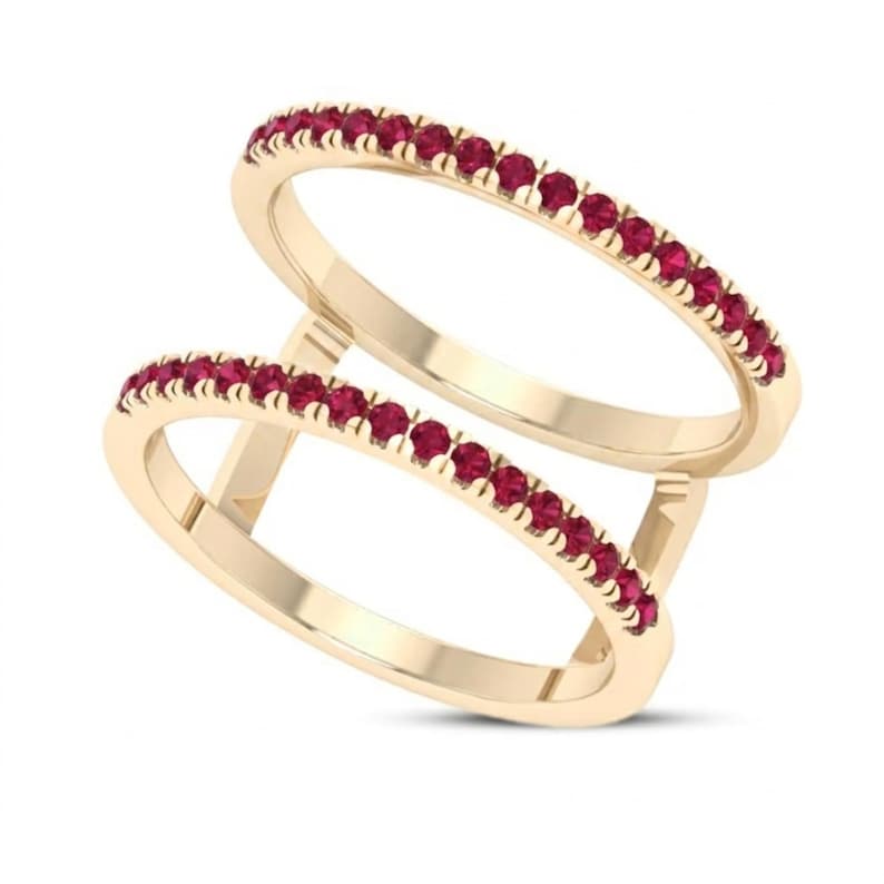 Pu&ograve; includere: Un anello a doppia fascia con una fascia color oro e una fila di piccole pietre preziose rosse. L'anello ha un design moderno con due fasce parallele collegate da supporti verticali.