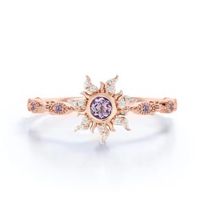 Puede incluir: Un anillo de oro rosa con un diseño de sol, con una piedra preciosa central de color púrpura claro. Los rayos del sol están acentuados con pequeñas piedras preciosas blancas. La banda está adornada con pequeñas piedras preciosas púrpuras.