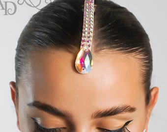 Puede incluir: Un adorno para la cabeza con una gema central iridiscente en forma de lágrima. El adorno está adornado con pequeños cristales brillantes. El diseño es elegante y adecuado para ocasiones especiales.