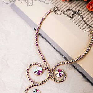 Puede incluir: Un collar de oro con diamantes de imitaci&oacute;n de color p&uacute;rpura iridiscente. El collar tiene forma de espiral con tres diamantes de imitaci&oacute;n grandes.