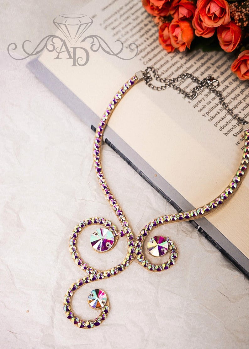 Puede incluir: Un collar de oro con diamantes de imitaci&oacute;n de color p&uacute;rpura iridiscente. El collar tiene forma de espiral con tres diamantes de imitaci&oacute;n grandes.