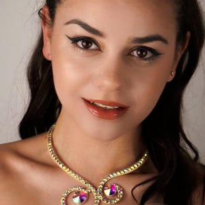 Puede incluir: Una mujer lleva un collar de oro con diamantes de imitaci&oacute;n iridiscentes. El collar es un dise&ntilde;o delicado y en espiral con tres diamantes de imitaci&oacute;n grandes en el centro.
