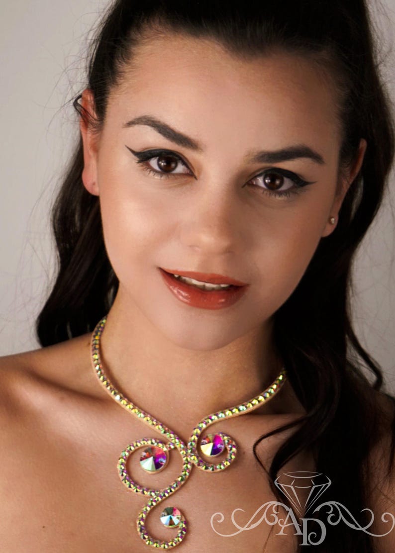 Puede incluir: Una mujer lleva un collar de oro con diamantes de imitaci&oacute;n iridiscentes. El collar es un dise&ntilde;o delicado y en espiral con tres diamantes de imitaci&oacute;n grandes en el centro.