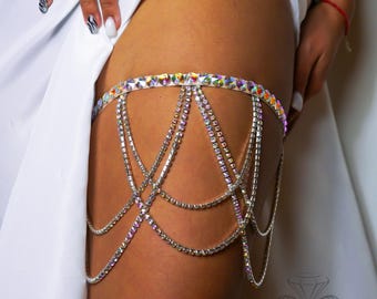 May include: A leg garter featuring a band of iridescent, multi-faceted crystals. Multiple draped strands of clear, sparkling rhinestones hang from the main band in a layered, scalloped pattern, creating a decorative accessory for the upper thigh.