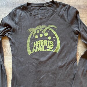 May include: A dark gray long-sleeved t-shirt with a green graphic of palm trees and the text "HARRIS WALZ".