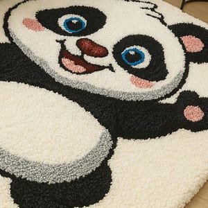 May include: A rectangular rug featuring a smiling panda bear design. The rug has a white background with black, gray, pink, and blue accents. The panda's face and body are prominently displayed, creating a playful and inviting aesthetic.