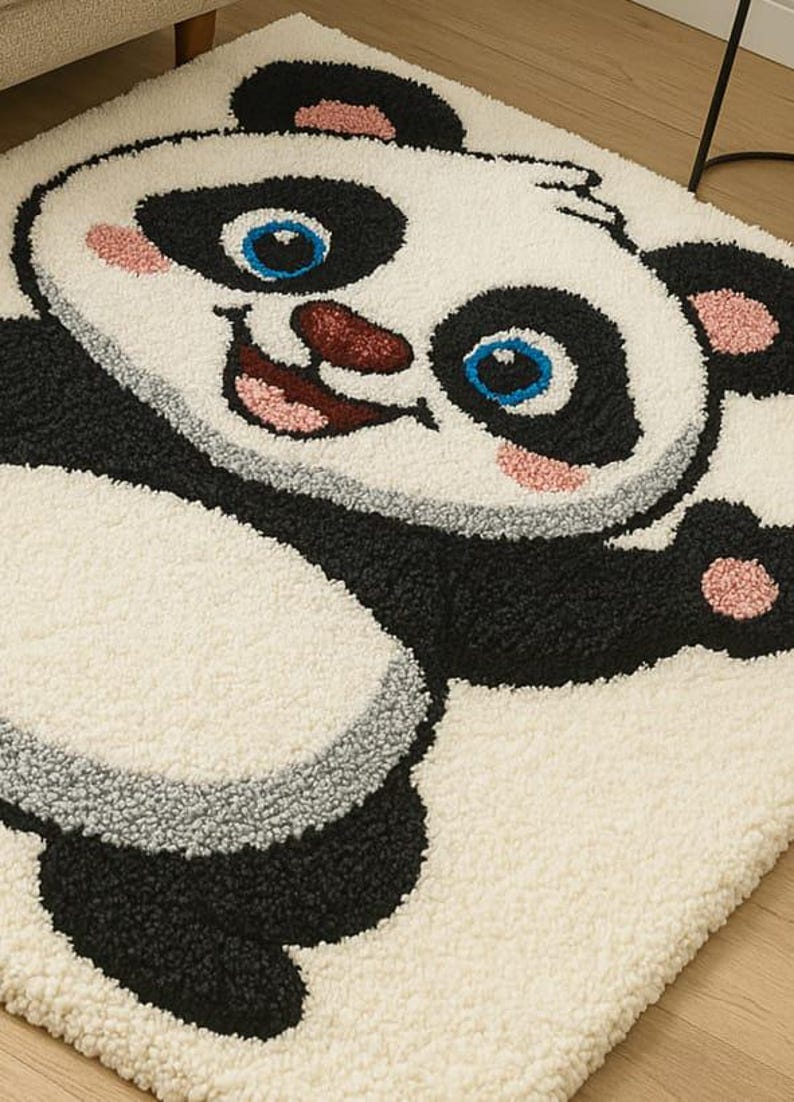 May include: A rectangular rug featuring a smiling panda bear design. The rug has a white background with black, gray, pink, and blue accents. The panda's face and body are prominently displayed, creating a playful and inviting aesthetic.