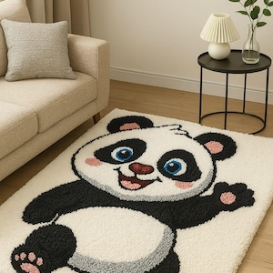 May include: A white, shaggy rug featuring a large, cartoon panda bear design. The panda has black and white fur, pink accents, and blue eyes. The rug is placed on a wooden floor, with a beige sofa and side table in the background.