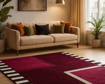 May include: A modern living room featuring a beige sofa with colorful throw pillows, a burgundy geometric rug with black and white stripes, and a large abstract painting. A gold floor lamp and potted plants add to the decor.