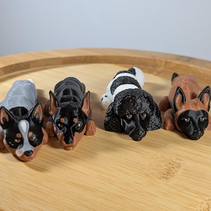 May include: Four small, 3D printed dog figurines. The dogs are lying down and are made of black, brown, white, and gray plastic.