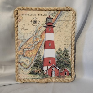 May include: A nautical-themed wall decor featuring a red and white lighthouse with a rope border. The lighthouse is set against a background of a vintage nautical map with the text "Assateague Island" and "Assateague Light".