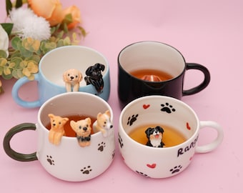 May include: Four ceramic mugs with dog figurines inside. The mugs are in various colors: light blue, black, and white. The white mugs have paw prints and red hearts. The mugs are filled with a liquid, and the background is pink.