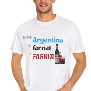 May include: White t-shirt with the words "Hecho en Argentina con Fernet y Pasion" in blue and red text. The shirt also features a graphic of a Fernet bottle and a small bottle of Coca-Cola.