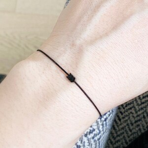Puede incluir: Un brazalete simple de cuerda negra con un pequeño dije de flecha negra.