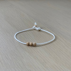 May include: A white string bracelet with three wooden beads.