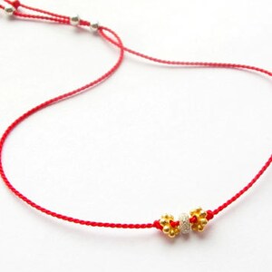 May include: A red string bracelet with two gold beads and a silver bead in the center.