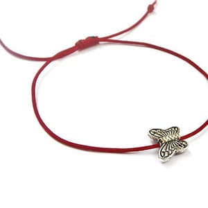 Puede incluir: Un brazalete de cuerda roja con un dije de mariposa plateado.