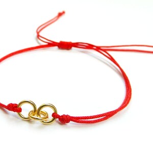 May include: A red string bracelet with a gold double circle charm.