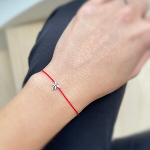 May include: A red string bracelet with a silver dragonfly charm.