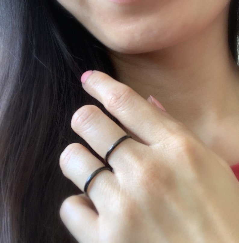 May include: Three black metal rings worn on a person's fingers. The rings are simple and minimalist in design.