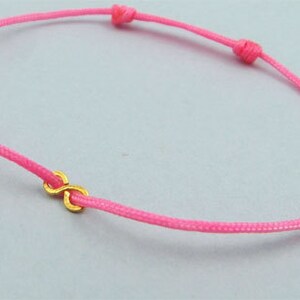 May include: A pink string bracelet with a gold infinity symbol charm.