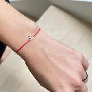 May include: A red string bracelet with a silver charm in the shape of a flower.