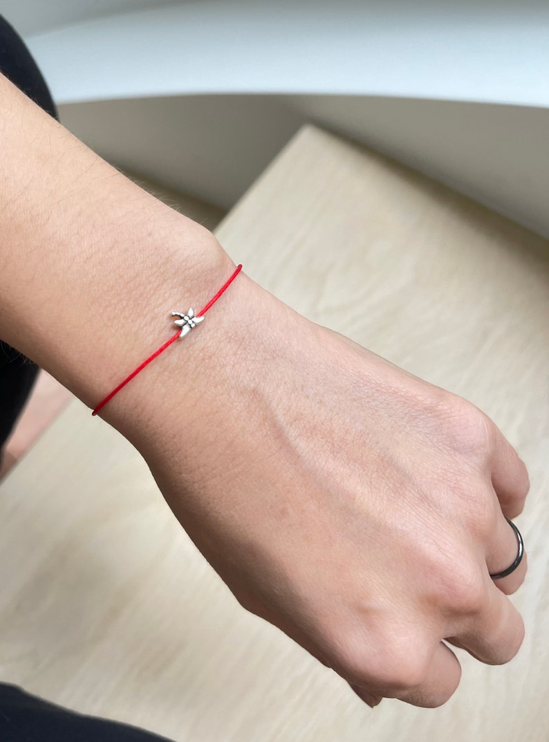 May include: A red string bracelet with a silver charm in the shape of a flower.