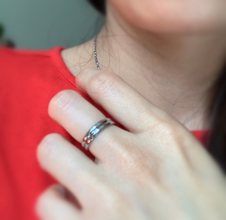 May include: A silver ring with three bands, worn on a finger.