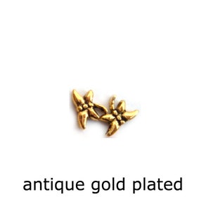 May include: Two antique gold-plated flower charms. The flowers are stylized and have five petals.